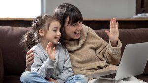 A mother and daughter waving at a laptop screen during a video call